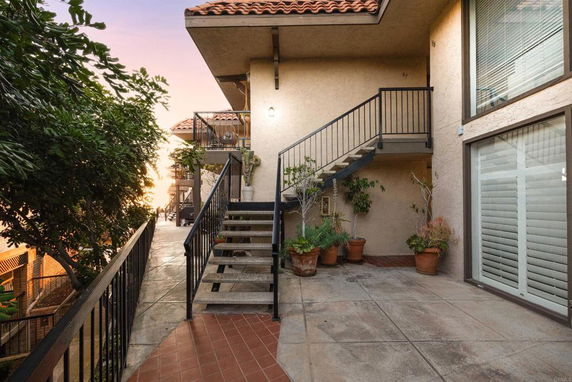 Exterior view of a multi-story building with a stairway and potted plants.