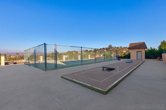 Outdoor play area with a fenced tennis court and shuffleboard in a recreational space.