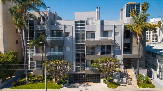 Front view of a multi-story apartment building with balconies and palm trees.