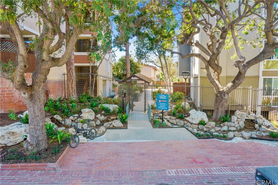 Gated entrance with brick pathway and surrounding greenery leading to residential buildings.