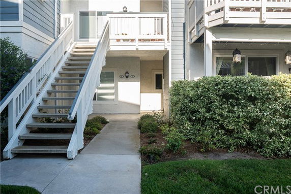 Front view of a two-story residential building with an exterior staircase and small garden area.
