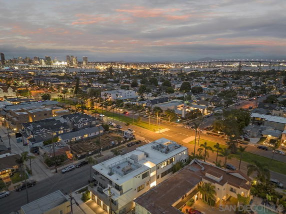 Aerial panoramic view of a cityscape during dusk with illuminated buildings and streets.