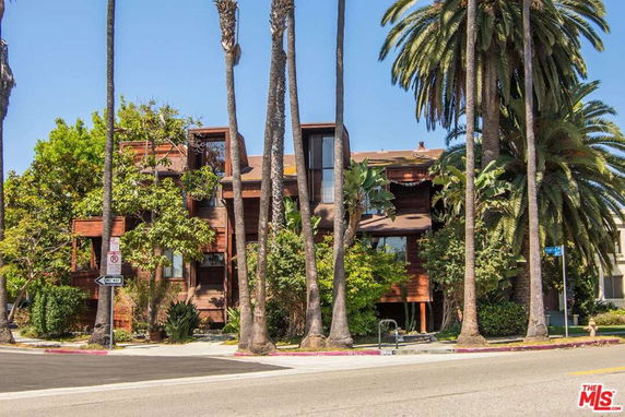 Front view of a multi-story house with a wooden exterior surrounded by tall palm trees.