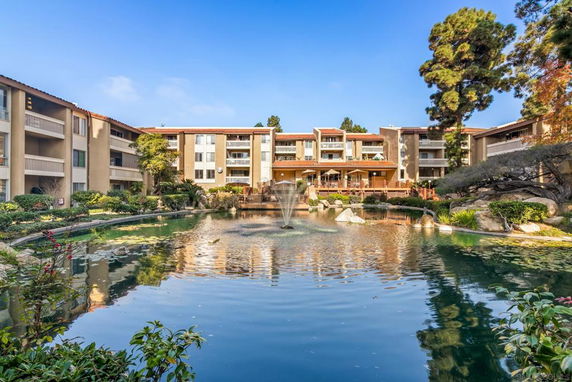 Front view of a multi-story residential building with balconies and surrounding landscaped gardens.