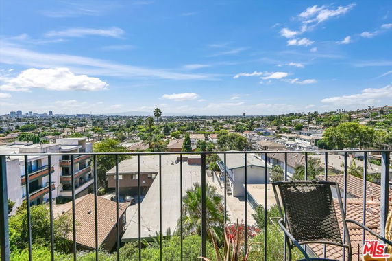 Panoramic view of a cityscape from a balcony with distant buildings and clear blue sky.