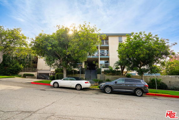 Front view of a multi-story residential building with balconies and surrounding trees.