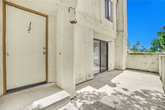 Front view of a building entrance with a door labeled '1 2' and a glass sliding door on a concrete patio.
