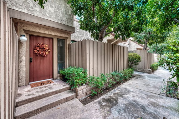 Front view of an entrance to a house with a wooden front door and surrounding fence.