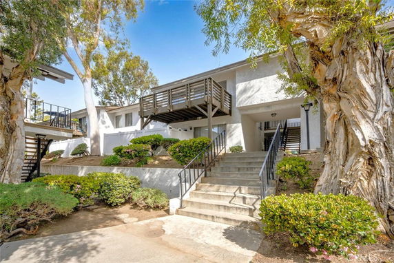 Front view of a two-story residential building with a staircase leading to the entrance and a balcony.