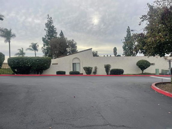 Front view of a single-story building with an arched entrance and surrounding shrubs.