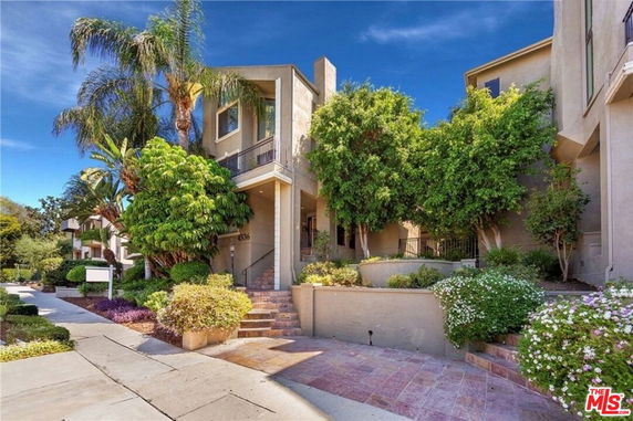 Front view of a multi-story house with stairs and lush greenery.