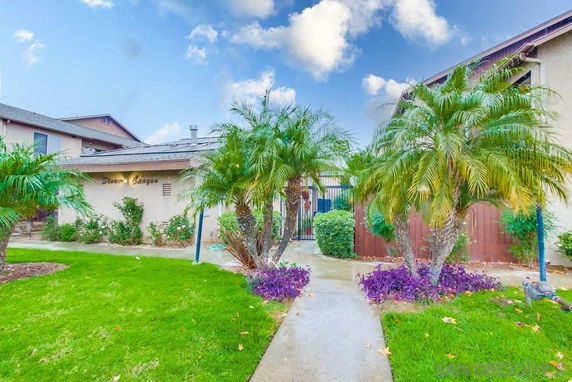 Front view of a building with palm trees and a sidewalk leading to an entrance.