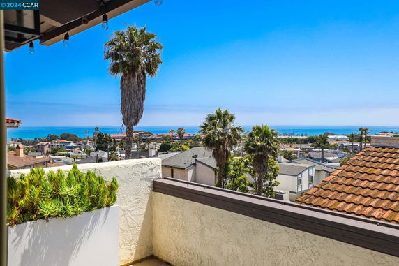 Wide angle view from a building balcony overlooking houses and the ocean in the distance.