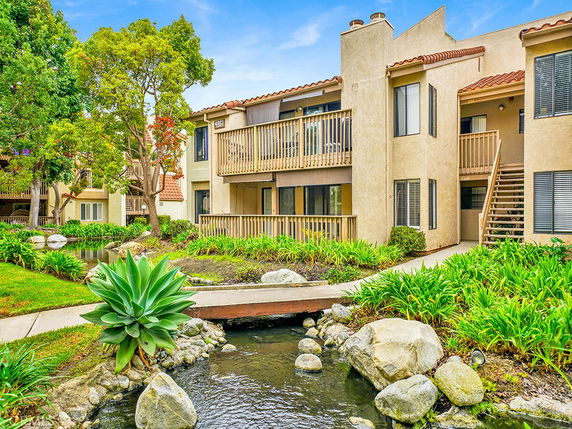 Front view of a multi-story residential building with balconies and surrounding greenery.