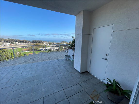 A tiled balcony area with a railing, offering a panoramic view of the surrounding landscape, including a glimpse of the ocean in the distance.