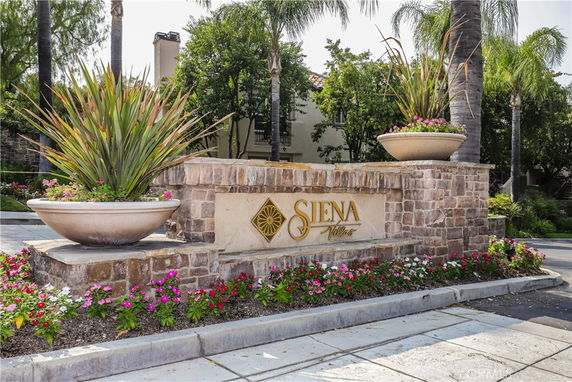 Front view of a stone wall entrance with decorative planters and a sign for Siena Villas.