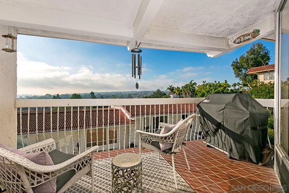 Balcony view overlooking rooftops and distant landscape, with outdoor furniture and grill.