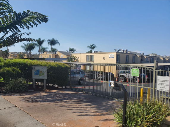 Exterior view of a gated community with a parking area and residential buildings.