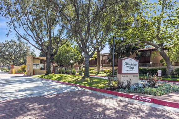 Entrance view of MacArthur Village Condominiums with a sign and guardhouse visible.