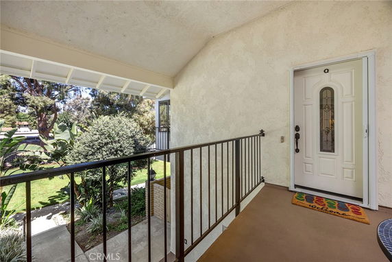 Entrance of a house with a view of gardens and trees, featuring a white door and railing.