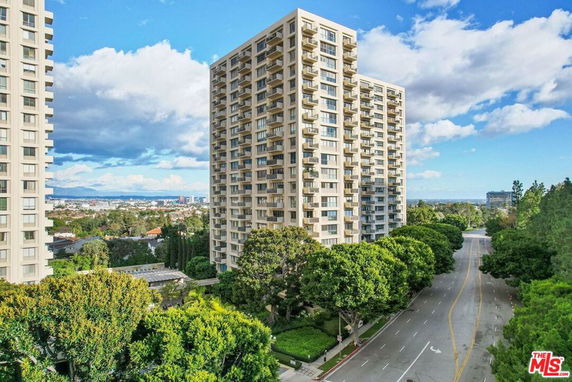 View of high-rise apartment buildings with surrounding trees and cityscape in the distance.