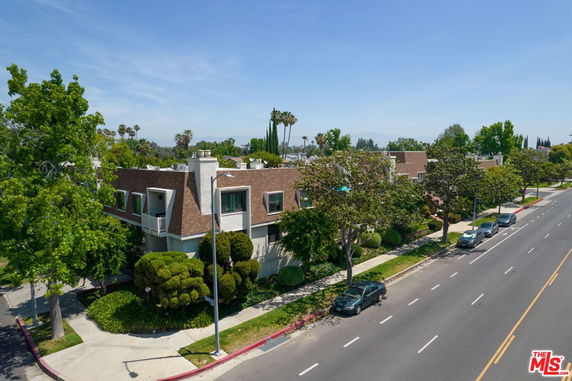 Aerial view of a residential building with sloped brown roofs on a tree-lined street.