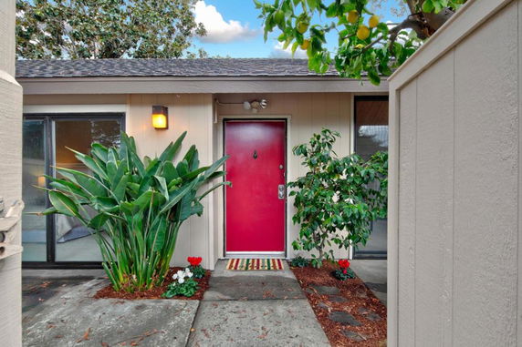 Front view of a single-story house with a red door and plants on either side.