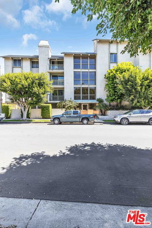 Front view of a multi-story residential building with large windows and parked cars in front.