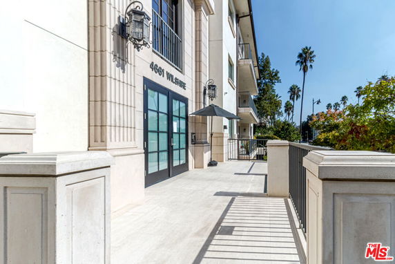 Front view of a multi-story building with large glass doors and a shaded patio area.