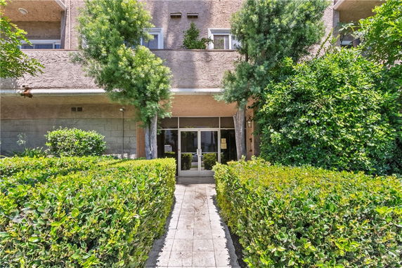 Front view of a multi-story building with a central entrance surrounded by greenery.