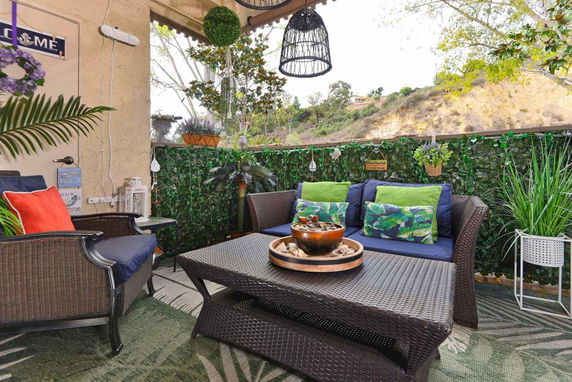 Outdoor patio area with wicker furniture and decorative plants, overlooking a hillside.