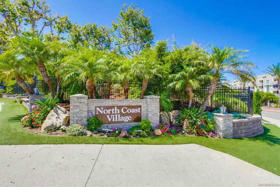 Front view of North Coast Village entrance with a stone sign and lush greenery.