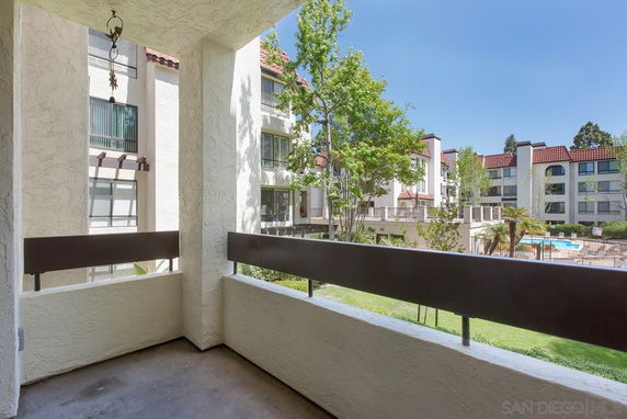 View from a balcony overlooking a residential complex with trees and swimming pool.