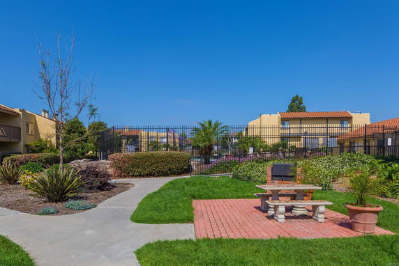 View of multiple residential buildings with tiled roofs, surrounded by landscaped gardens and a walkway.