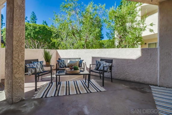 Outdoor seating area with chairs and cushions on a patio, surrounded by a wall and trees visible in the background.