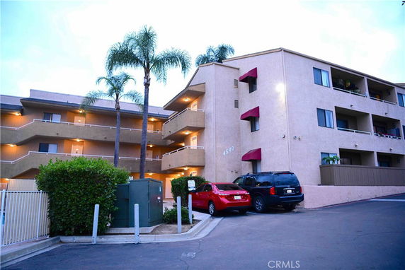 Front view of a multi-story apartment building with balconies and covered parking spaces.