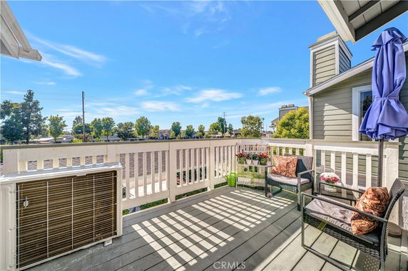 Rooftop deck with seating and plants, surrounded by a railing, overlooking trees and buildings.
