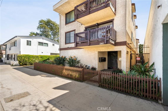 Front view of a multi-story apartment building with balconies and a small fenced garden area.