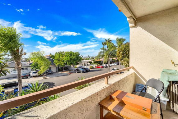 View from a balcony overlooking a residential street with parked cars and palm trees.