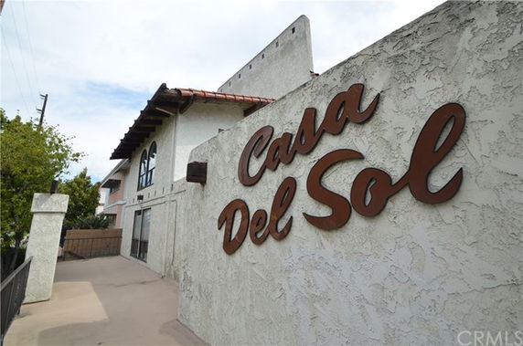Front view of a building with a textured white exterior and wooden sign reading 'Casa Del Sol'.