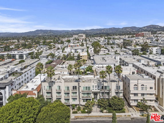 Aerial view of a cityscape with multiple residential buildings and palm trees, with mountains in the background.