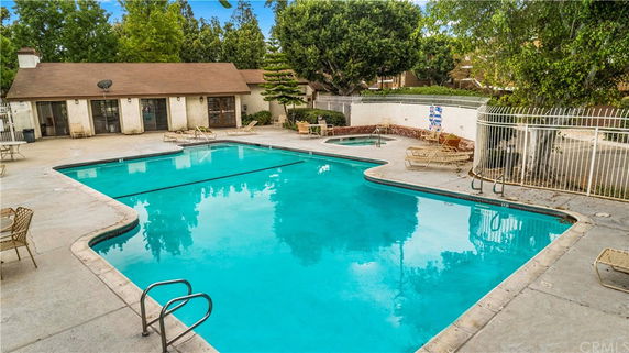 Outdoor swimming pool area with adjacent building and surrounding trees.