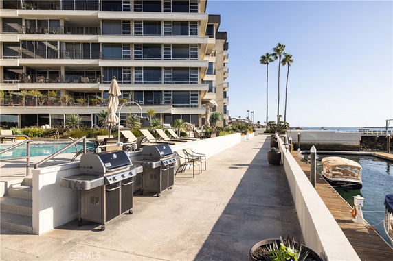 Outdoor area of a modern apartment building with a swimming pool and barbecue grills by the walkway.