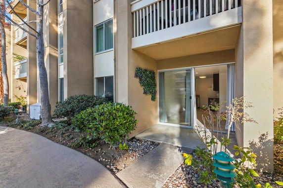 Front view of a multi-story apartment building with a balcony and sliding glass door.