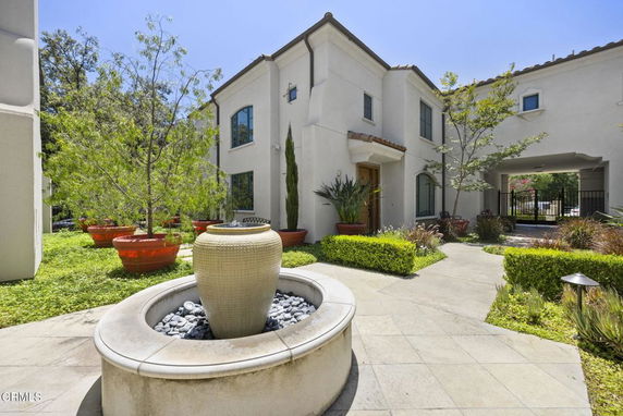 Front view of a two-story house with arched windows and a courtyard featuring a decorative planter.