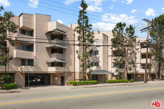 Front view of a multi-story apartment building with balconies and a gated entrance.
