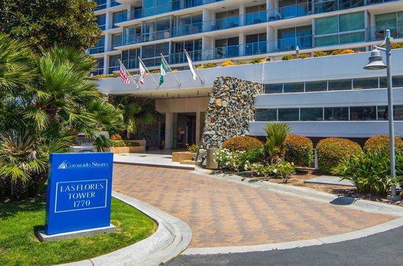 Front view of a multi-story building with a stone entryway and several flags displayed.