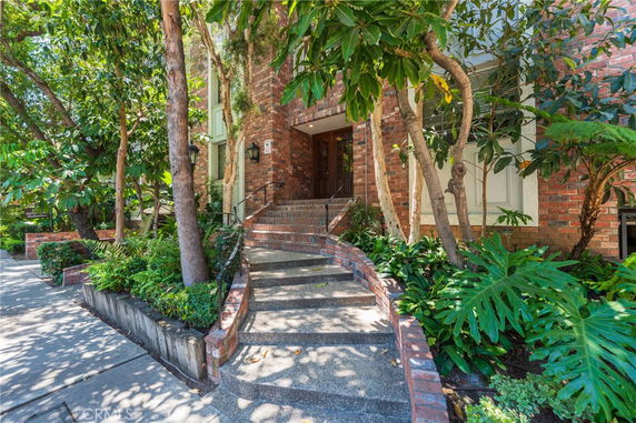 Front view of a brick building entrance with stairs and greenery.