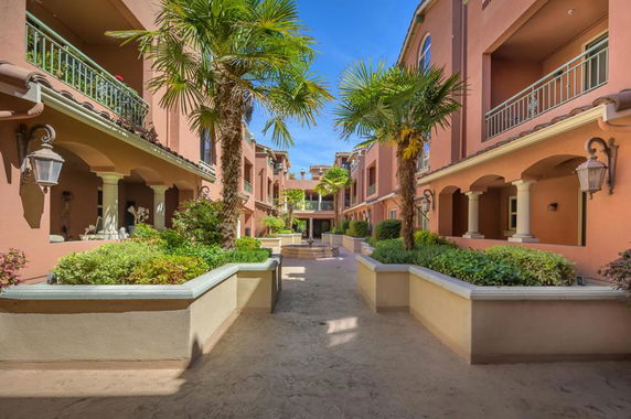View of a two-story building with balconies, decorative pillars, and palm trees.