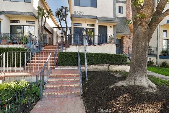 Front view of a multi-story townhouse with stairs leading to the entrance.